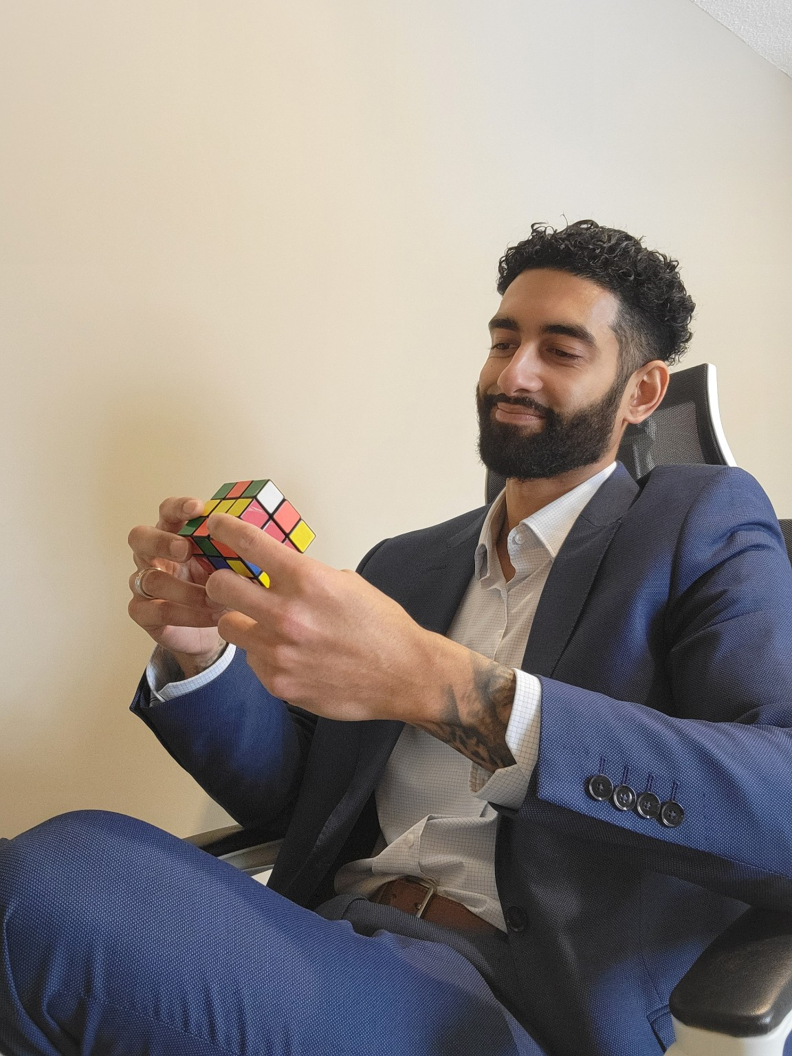 Joshua Jaipaul seated in a chair wearing a blue suit and holding a Rubik's Cube